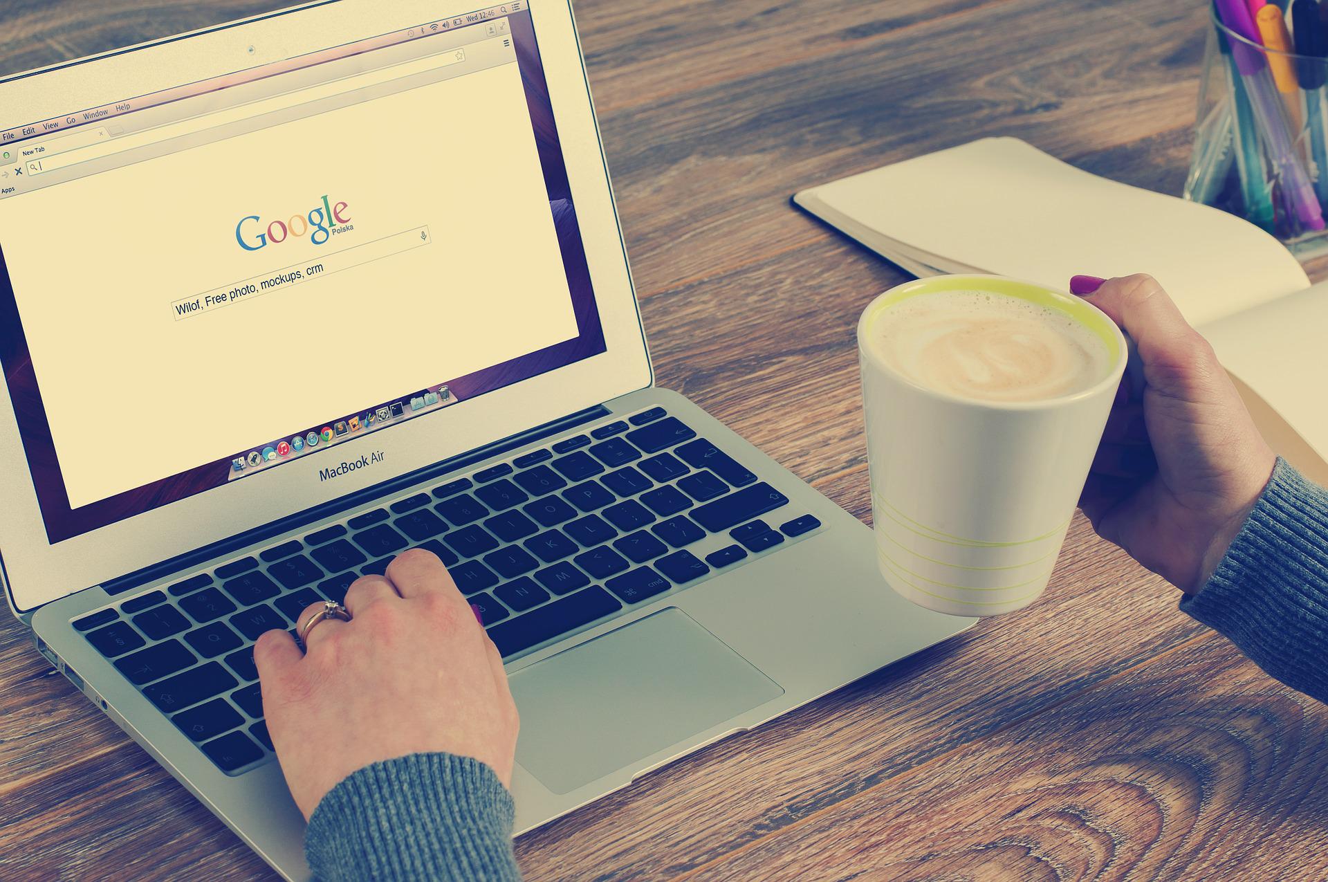Personne qui lance une recherche sur Google depuis un ordinateur portable, une tasse de café à la main
